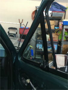 A green 1980s Ford truck door with the interior panel removed, showing the vertical division bar and the triangular vent window frame being prepared for new rubber seals.