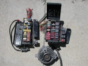 Two Ford power distribution blocks with wiring harnesses, a Mega-fuse, and a 3G alternator laid out for comparison, sourced from LKQ for a Bullnose truck wiring upgrade.