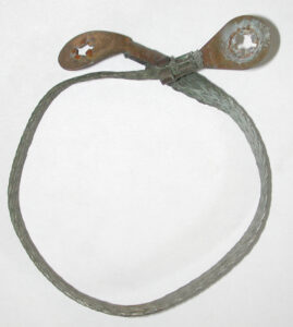 A weathered, braided metal ground strap with ring terminals, used to ground the hood to the firewall for the underhood light.