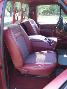 Two side-by-side images: the left shows a bare 1992-97 Ford seat mounting pan resting on a truck floor; the right shows a pair of high-back red vinyl bucket seats successfully installed in a white truck cab.