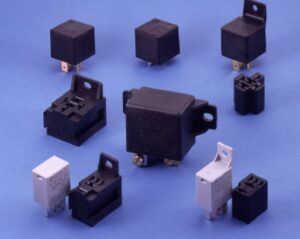 A collection of various black and grey automotive relays, including standard 5-pin Bosch units and high-capacity 50-amp versions from Chief Enterprises, illustrating different mounting tabs and pin configurations.