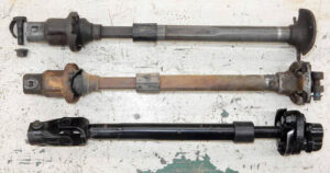 A comparison photo of three steering shafts: two original Bullnose units with split boots and one 1988-1991 direct-replacement unit.