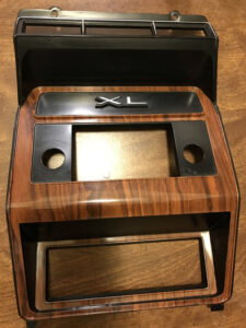A high-gloss, restored Rosewood plastic dashboard bezel for a Ford truck. The woodgrain is a deep reddish-brown and the raised plastic edges have been painted with a highly reflective, chrome-like silver finish.