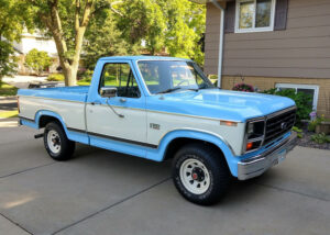 A light blue 1983 Ford F150 XL short bed with a black grille and white wagon wheels, featured in the 2020 Virtual Truck Show.