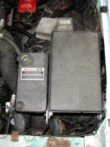 A photo of a black plastic storage box mounted to the driver-side inner fender of a Ford truck, with a coolant overflow bottle attached to its inner flank.