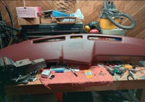Burgundy dash pad cover for 1980-86 Ford truck on a workbench surrounded by tools prior to installation.